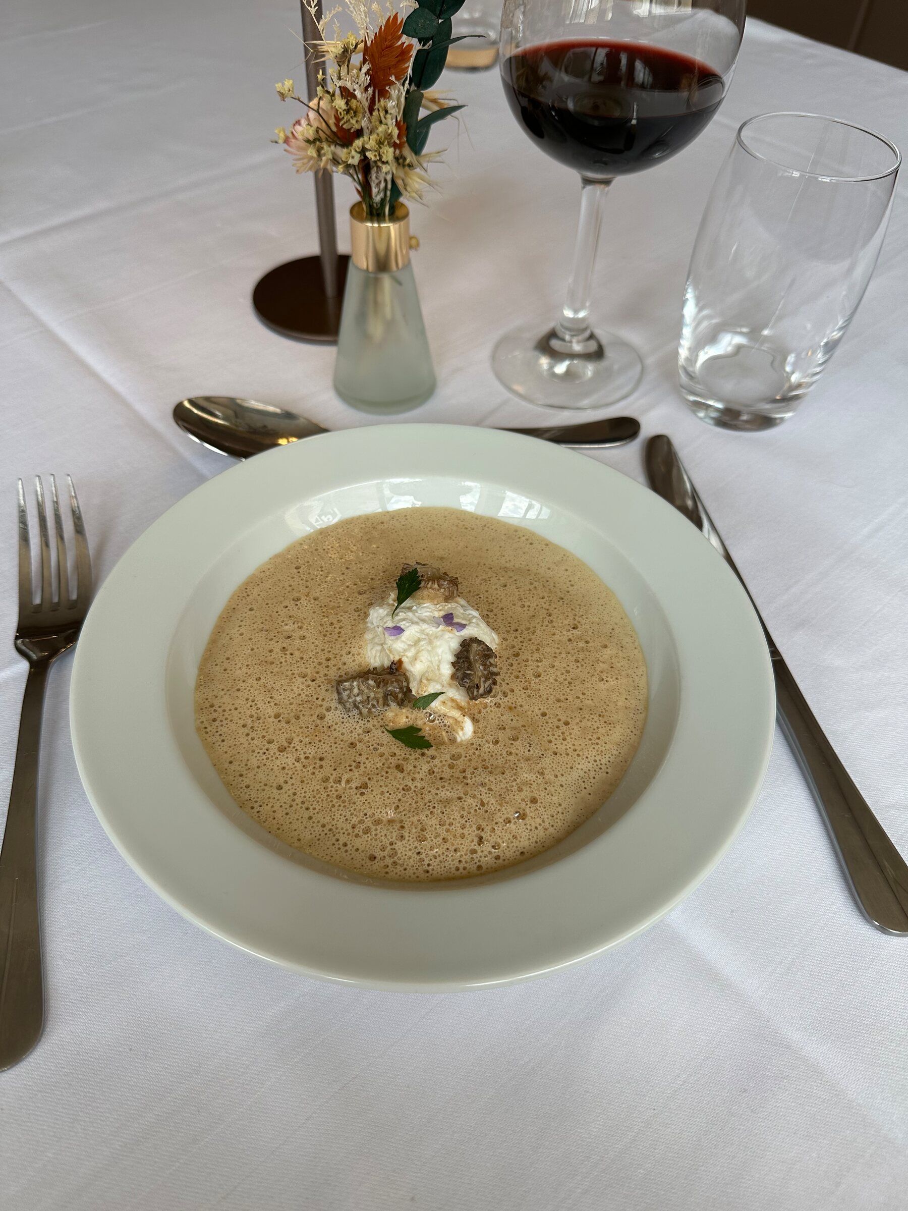 Velouté de champignons, crème légère et fleurs, servi avec un verre de rouge